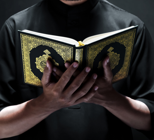 En person i mörka kläder håller i en bok med gulddetaljer mot en mörk bakgrund.