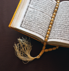 En uppslagen bok med en guldfärgad pärm visas tillsammans med ett radband och en tofs.