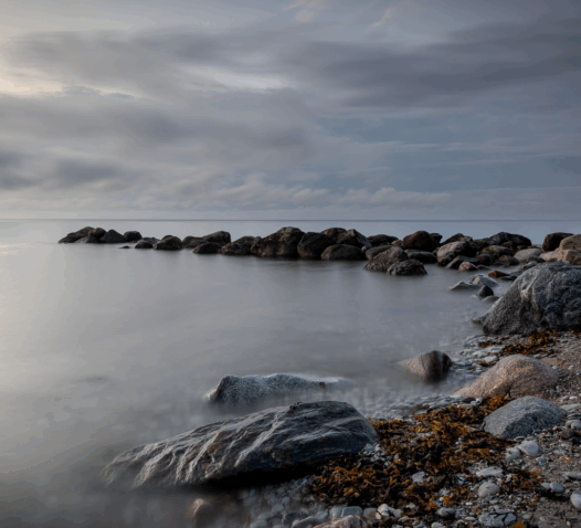 Kustlandskap med klippor och en lugn, molnig himmel.