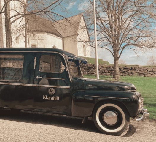 En svart begravningsbil står parkerad framför en kyrka.