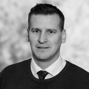 En man i kostym och slips ler svagt framför en suddig bakgrund.