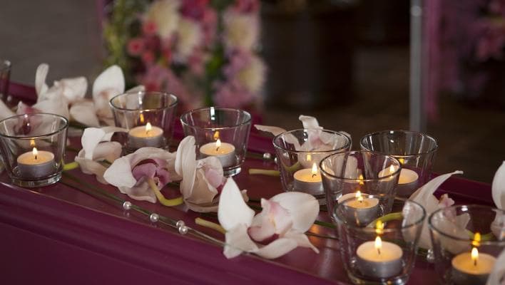 Värmeljus i glasbehållare står på ett bord dekorerat med vita och rosa orkidéer.