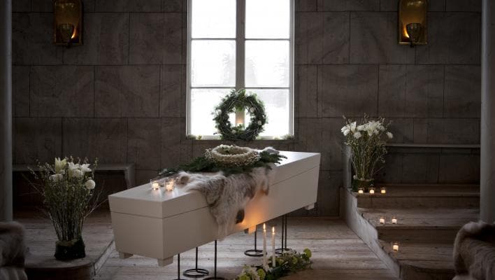 Vit kista dekorerad med ljus och blommor i ett rum med fönster och stenväggar.