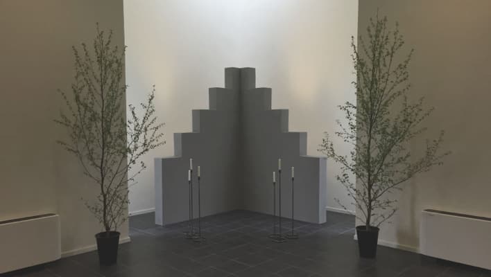 Två höga växter i krukor står på varsin sida av en grå trappformad struktur med flera nivåer.