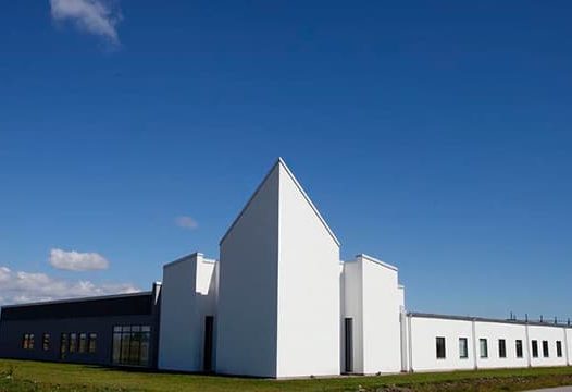 En modern byggnad med vit fasad och spetsigt tak under en klarblå himmel.